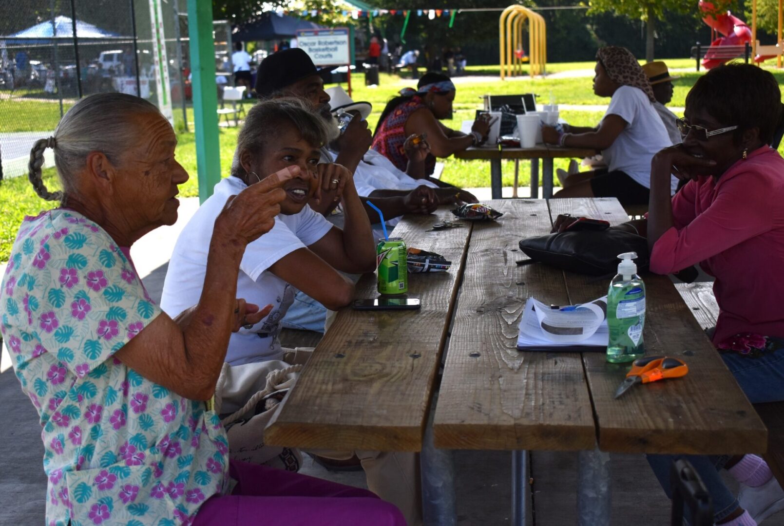 People eating together at an outdoor picnic table on a sunny day.