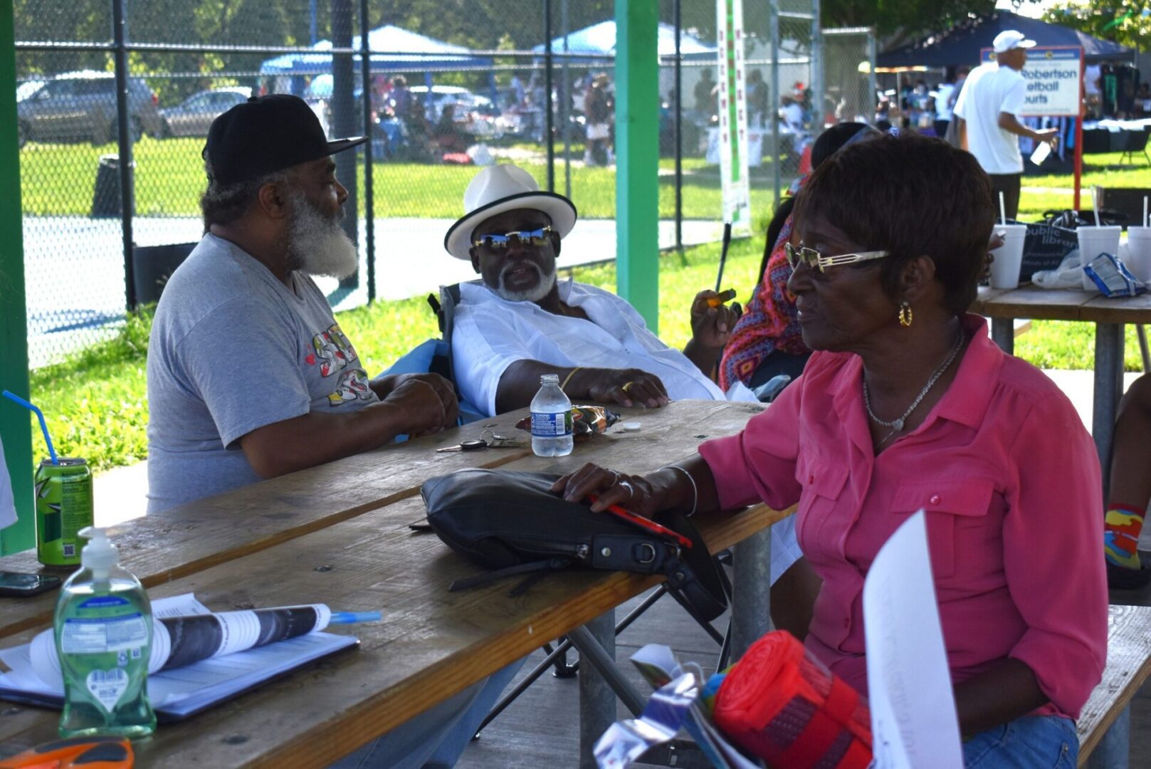 People sitting and chatting at an outdoor picnic table under a pavilion.