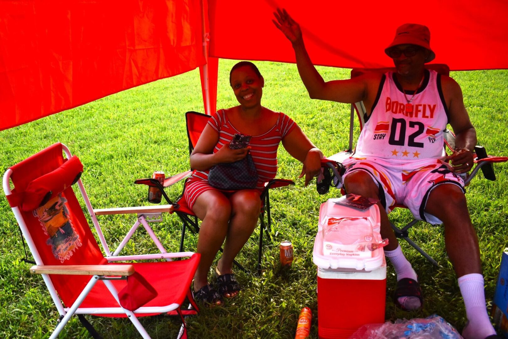 Two people relaxing under a red canopy on a sunny day.