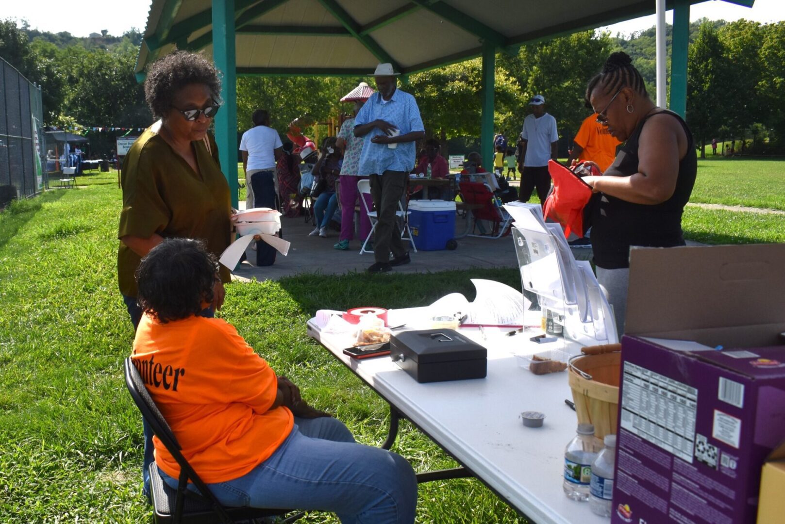 People gathered at an outdoor event with a table of refreshments and supplies.