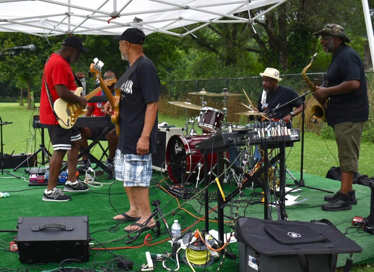A band performs outdoors under a white canopy with various instruments.