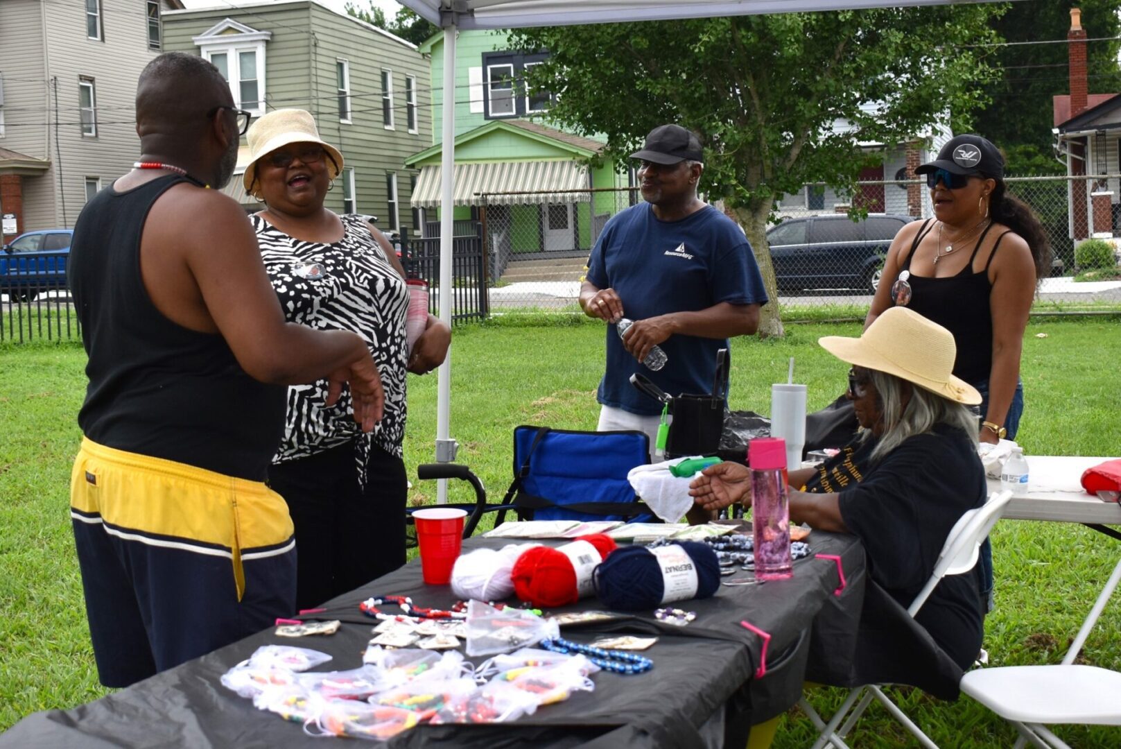 Group of people socializing outdoors with crafts and drinks on a table.